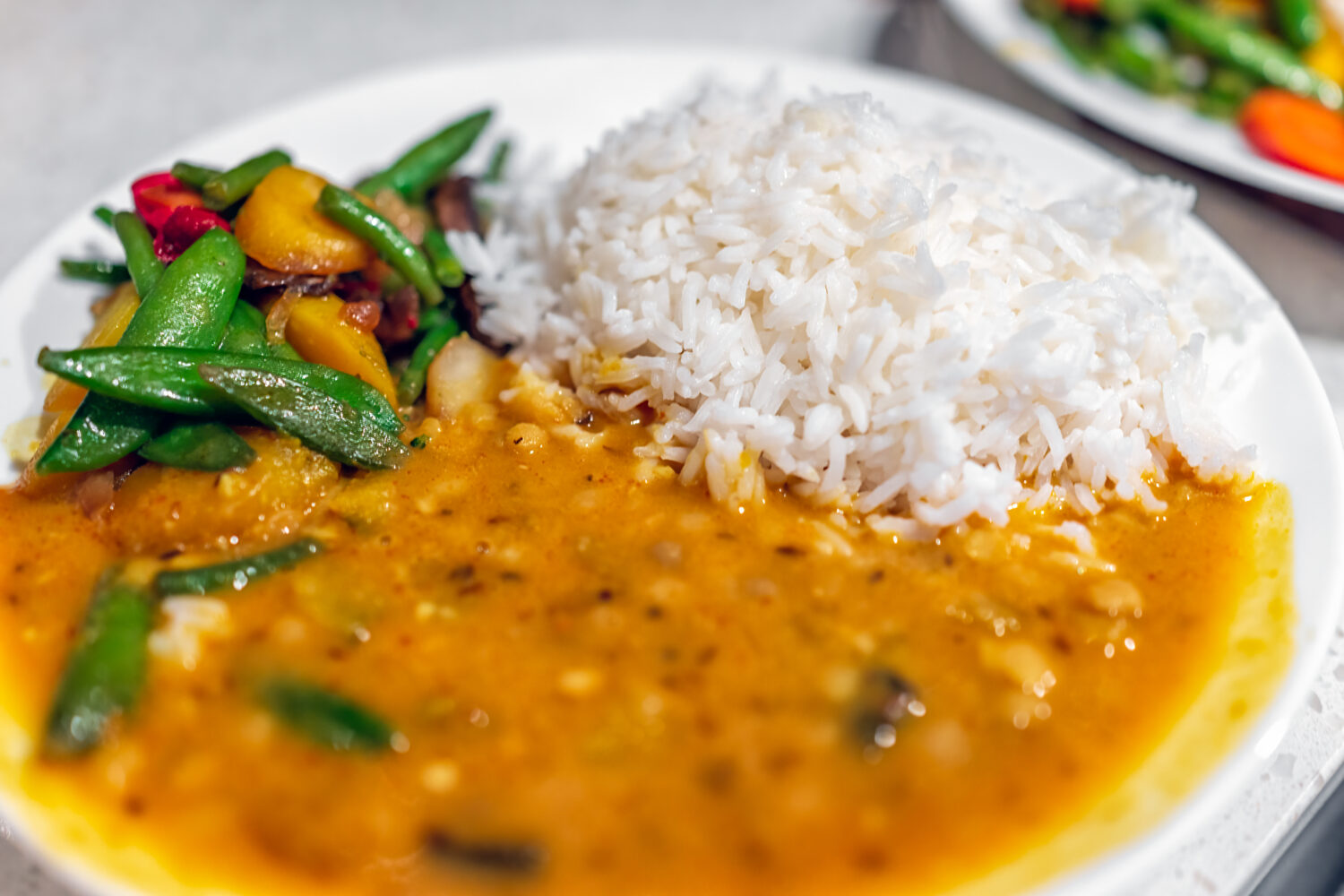 Macro closeup of orange curry healthy coconut squash dal Indian yellow split peas sauce food meal with white basmati rice on plate and vegetables as dinner