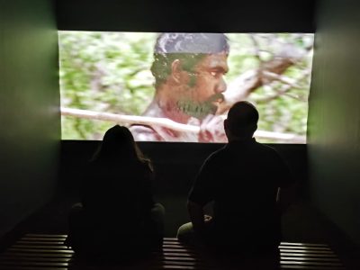 An audience member watches visual installation of aboriginal tribes