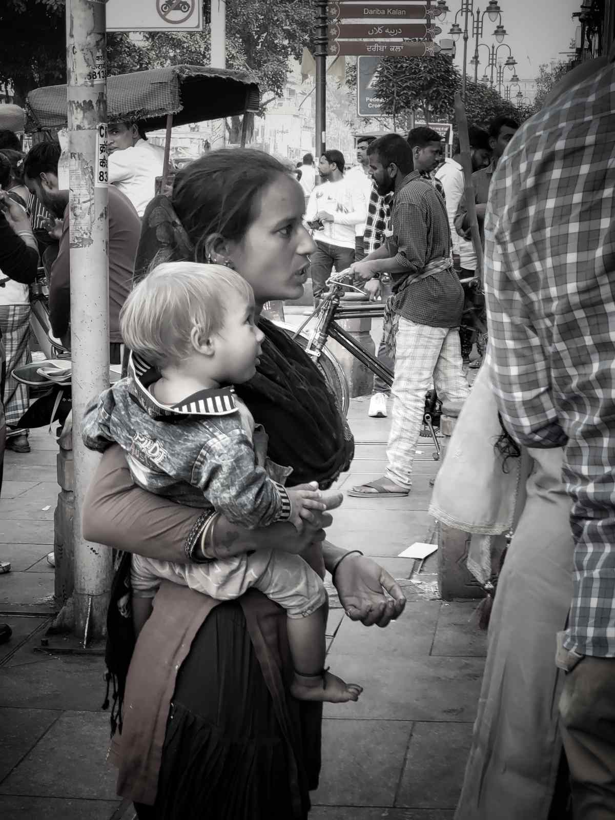 Desperate for Compassion: A mother cradles her baby, reaching out to strangers for help to feed her family. Her eyes reflect the relentless struggle and quiet desperation that define her daily life.