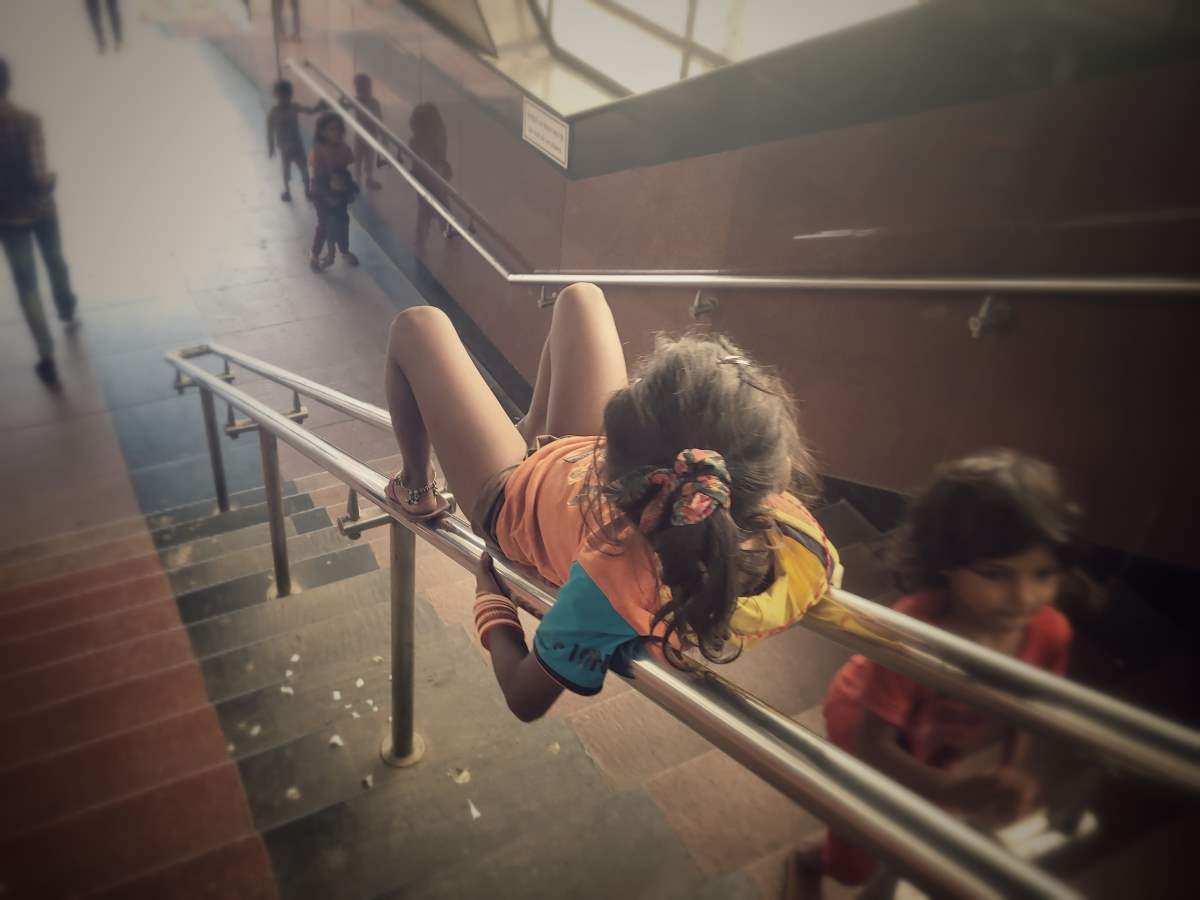 Joy in Small Spaces: A little girl lingers on the stairs of a metro station, absorbed in a moment of quiet play. In the midst of a busy world, she carves out a small space for childhood